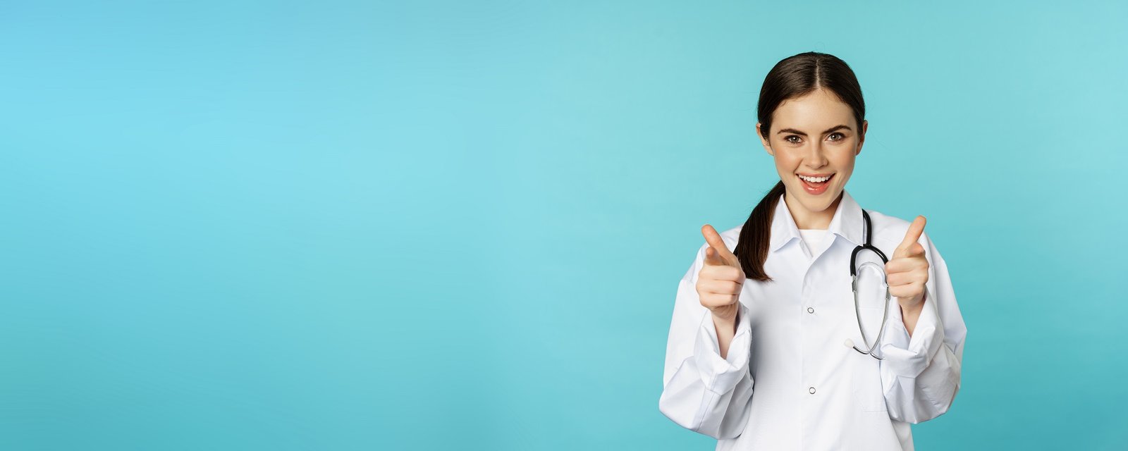 Enthusiastic woman doctor smiling, pointing fingers at camera, congratulating, inviting patients to clinic, standing over torquoise background Enthusiastic woman doctor smiling, pointing fingers at camera, congratulating, inviting patients to clinic, standing over torquoise background.
